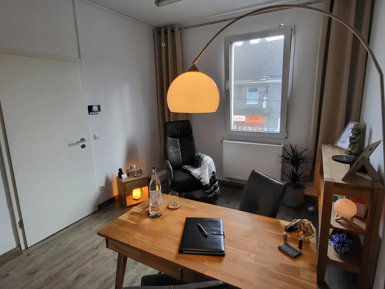 Praxisraum in Solingen mit Holztisch, Sitzplätzen und warmer Bogenlampe