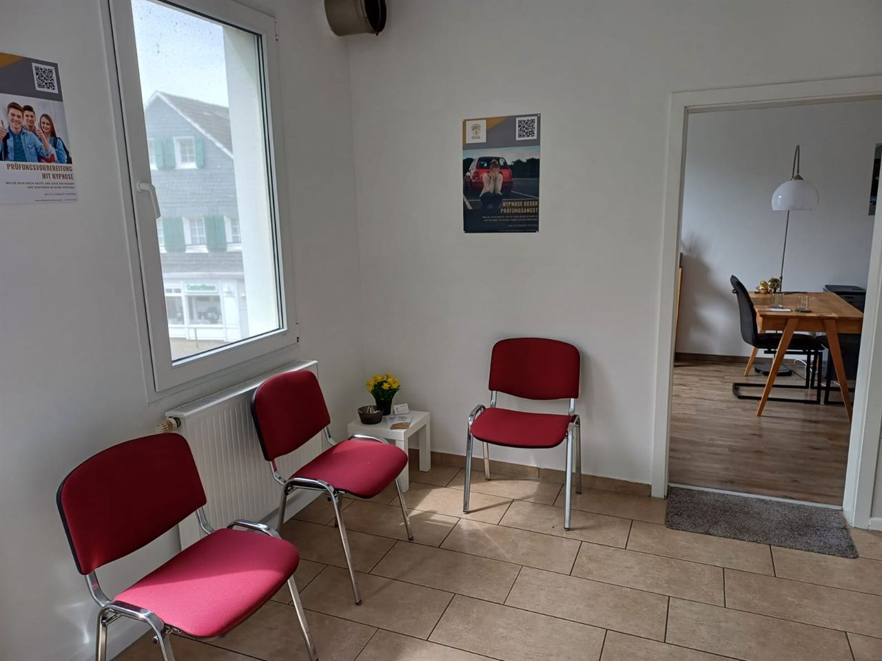 Heller Wartebereich mit drei roten Stühlen, Fenster und Durchgang zum Coachingraum